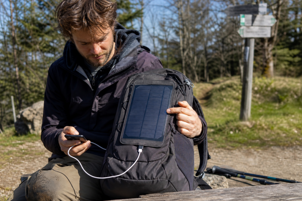 Wanderer lädt sein Smartphone mit einem markenfreien Solarrucksack [Bildinhalt mit KI erstellt]