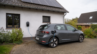 Elektroauto lädt an einer Wallbox neben einem Wohnhaus mit Photovoltaik. KI-Symbolbild. [Bildinhalt mit KI erstellt]