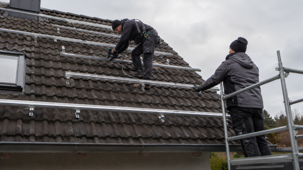 Gesicherter Dachdecker montiert Solarschienen auf gleichmäßig gesetzten Dachhaken [Bildinhalt mit KI erstellt]