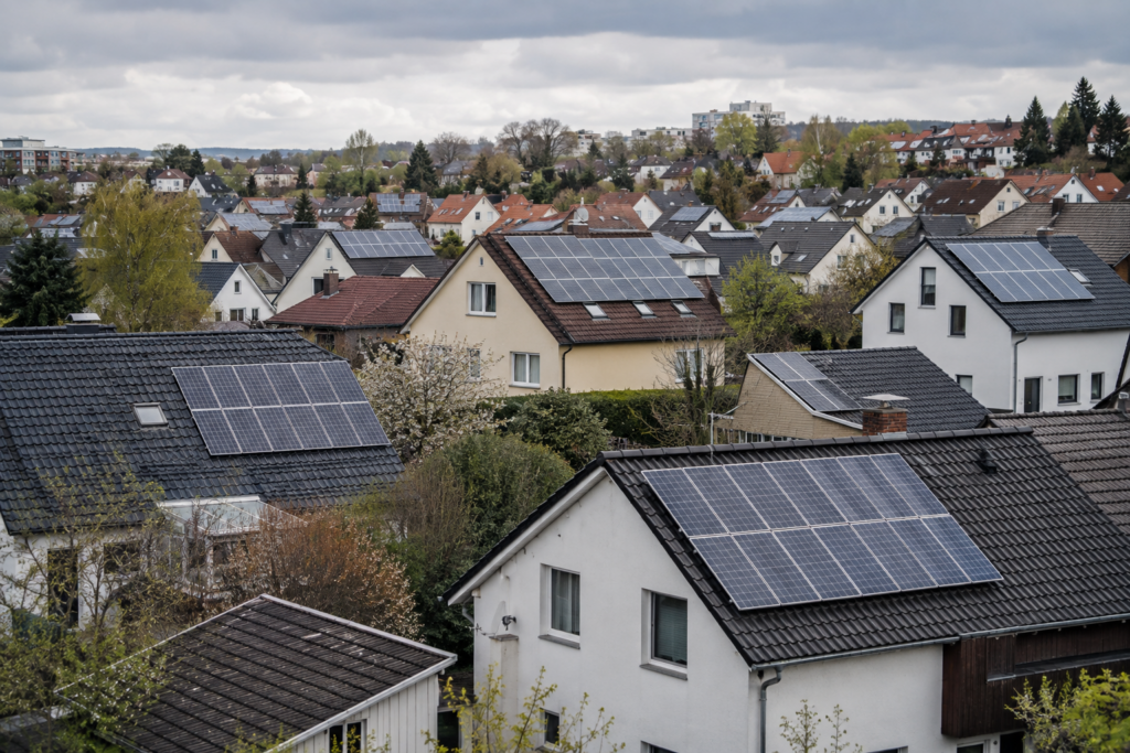 Photovoltaikanlagen auf unterschiedlichen Hausdächern in einem Wohngebiet. [Bildinhalt mit KI erstellt]